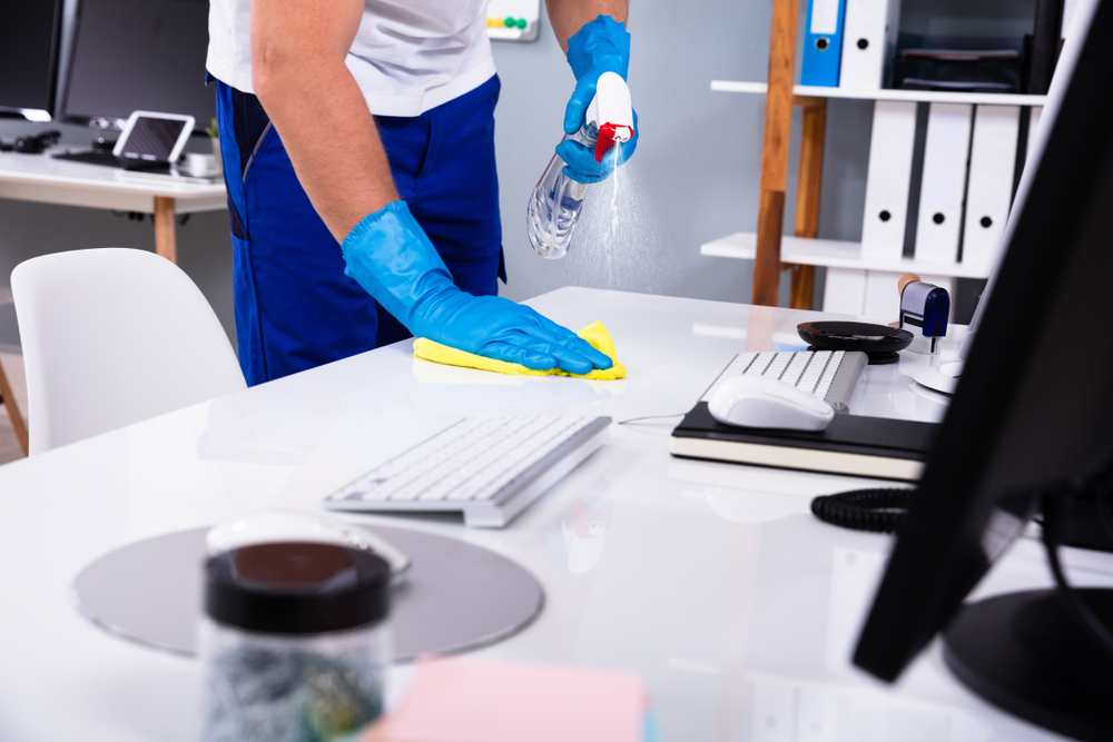 Staff sanitizing a modern office desk with spray and microfiber cloth