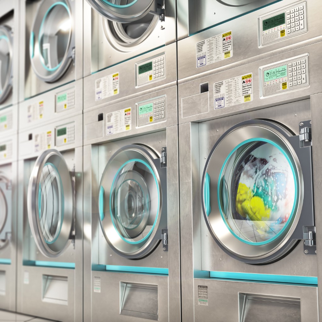 Row of stainless commercial laundry washers and dryers in operation